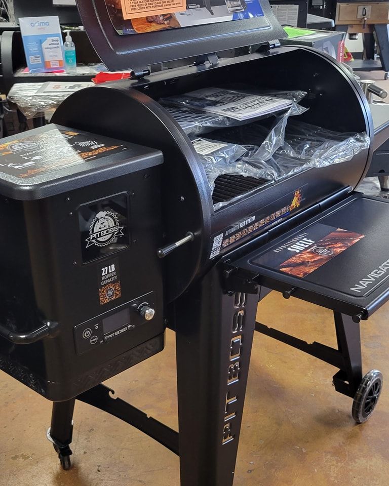 A black grill with the lid open is sitting on a wooden floor.