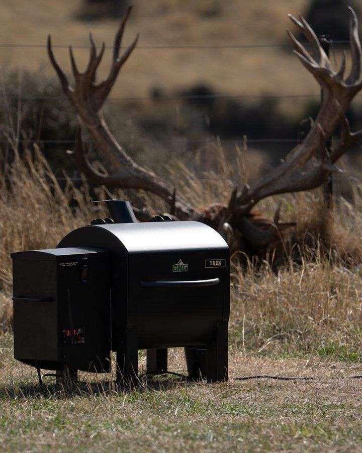 A large deer with antlers is standing next to a grill in a field
