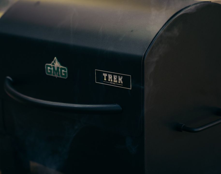 A close up of a gmg trek grill with smoke coming out of it.