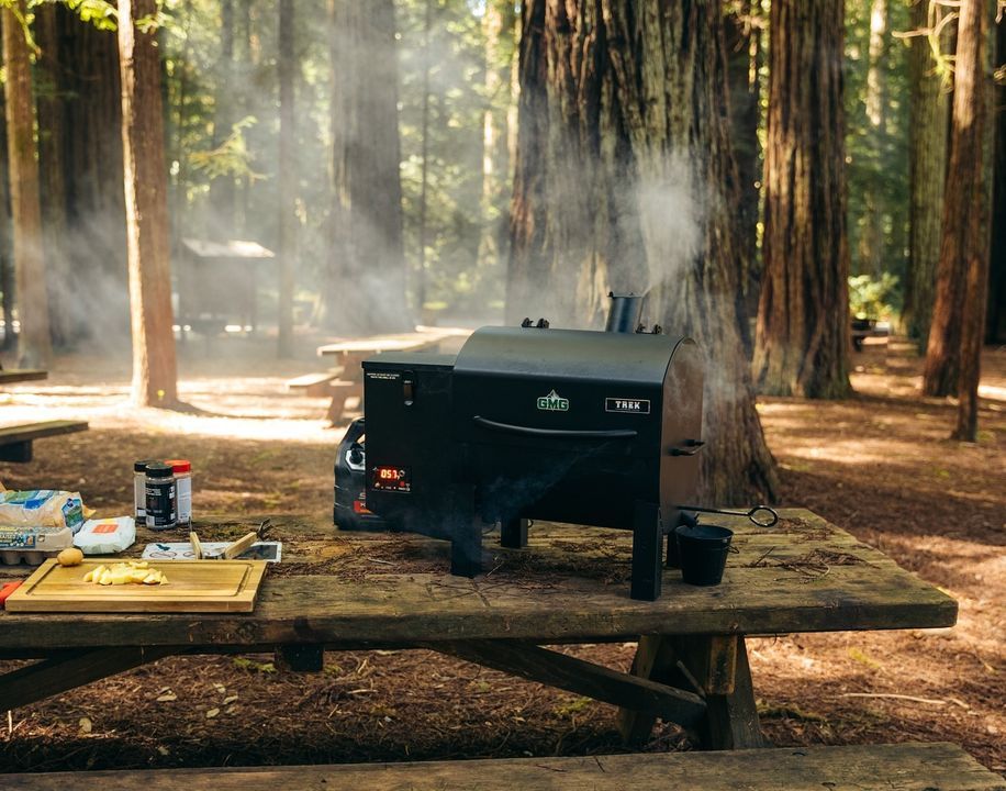 A picnic table with a grill on it in the woods.