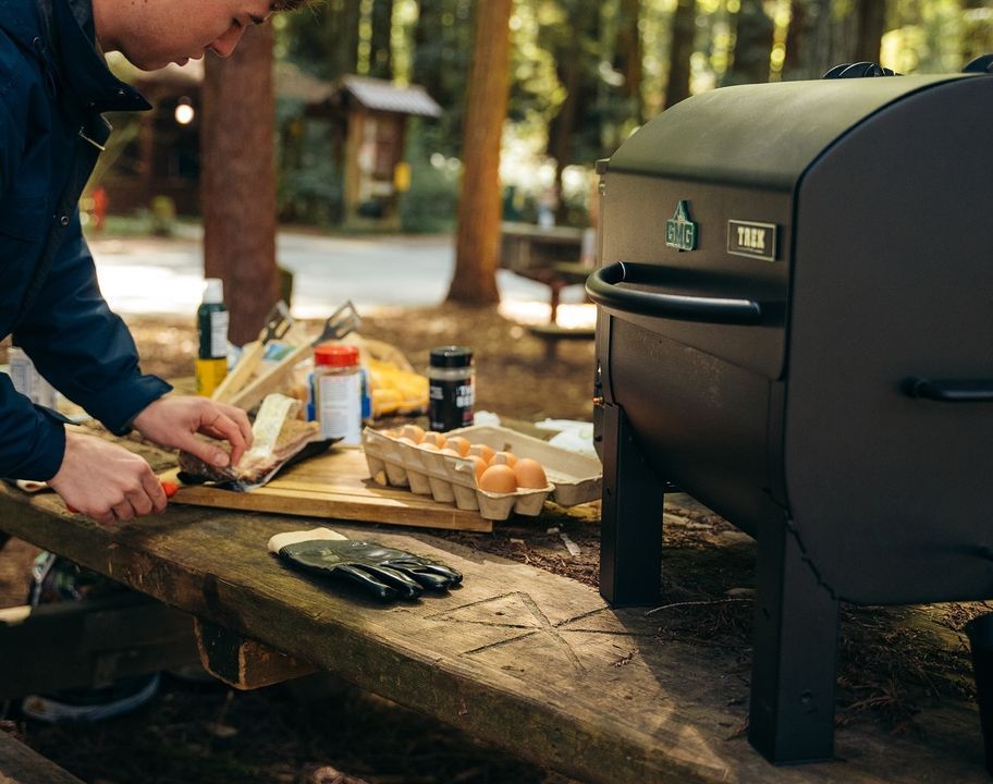 A man is cooking food on a grill in the woods.