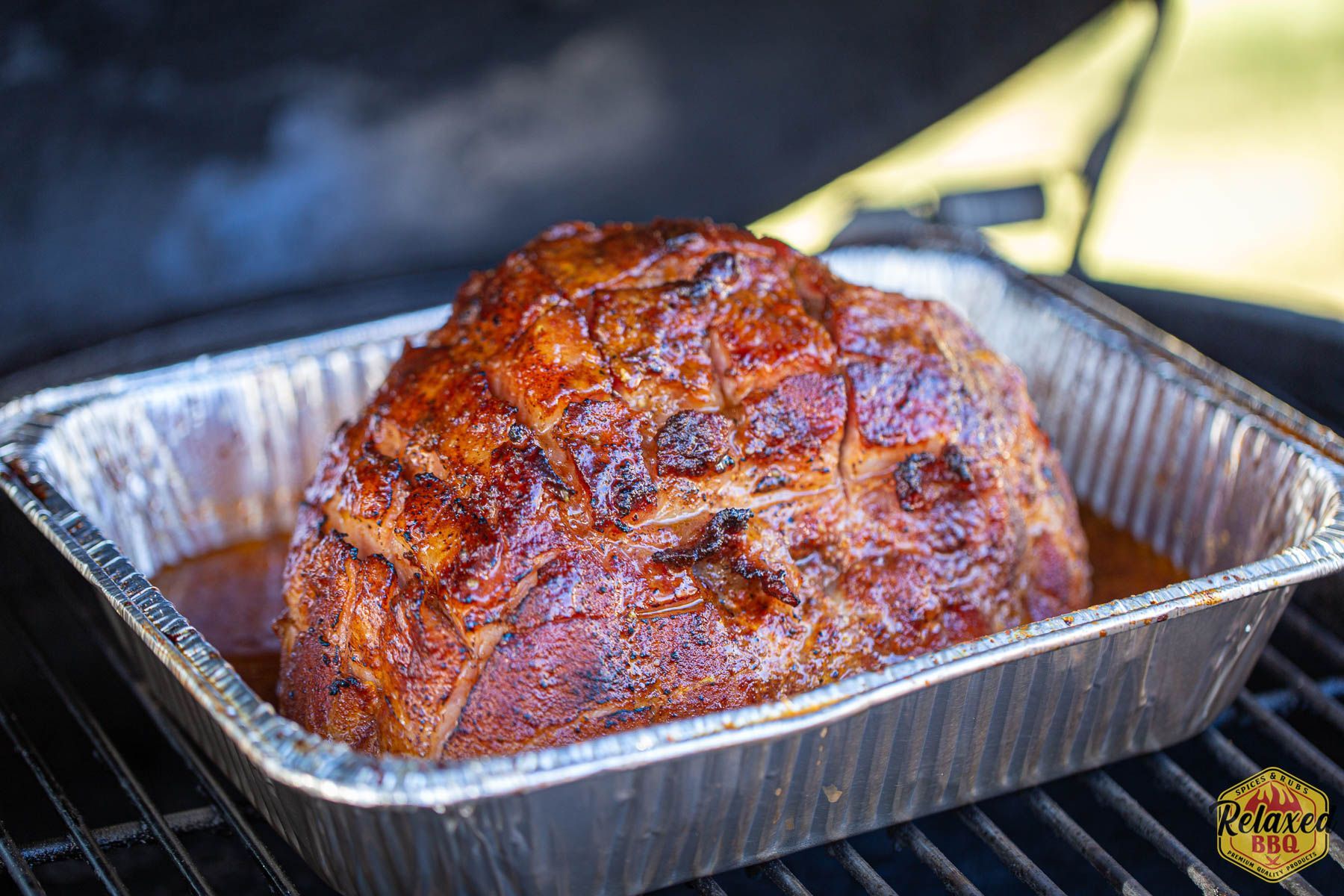 A large piece of meat is sitting in a tin foil pan on a grill.