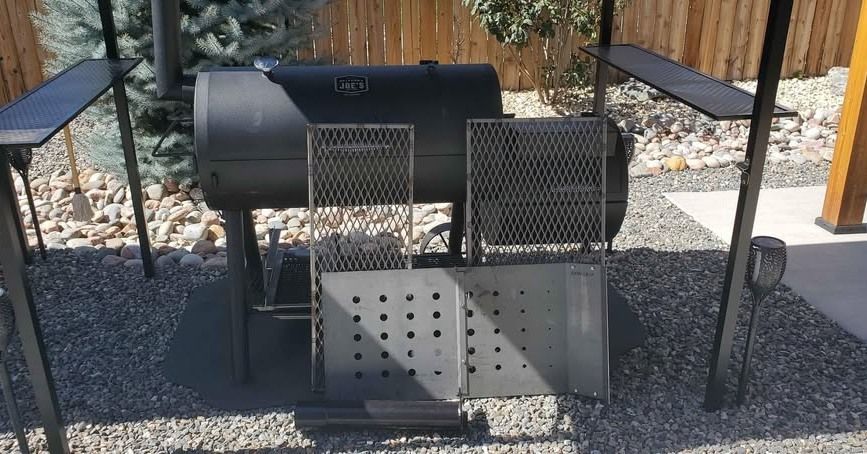 A black grill is sitting on top of a gravel patio next to a wooden fence.
