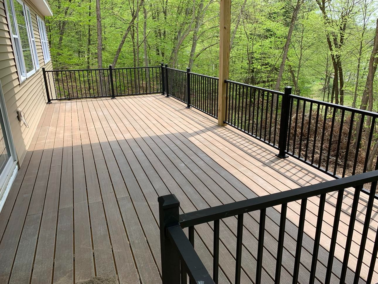 A wooden deck with black railings overlooks a wooded area.