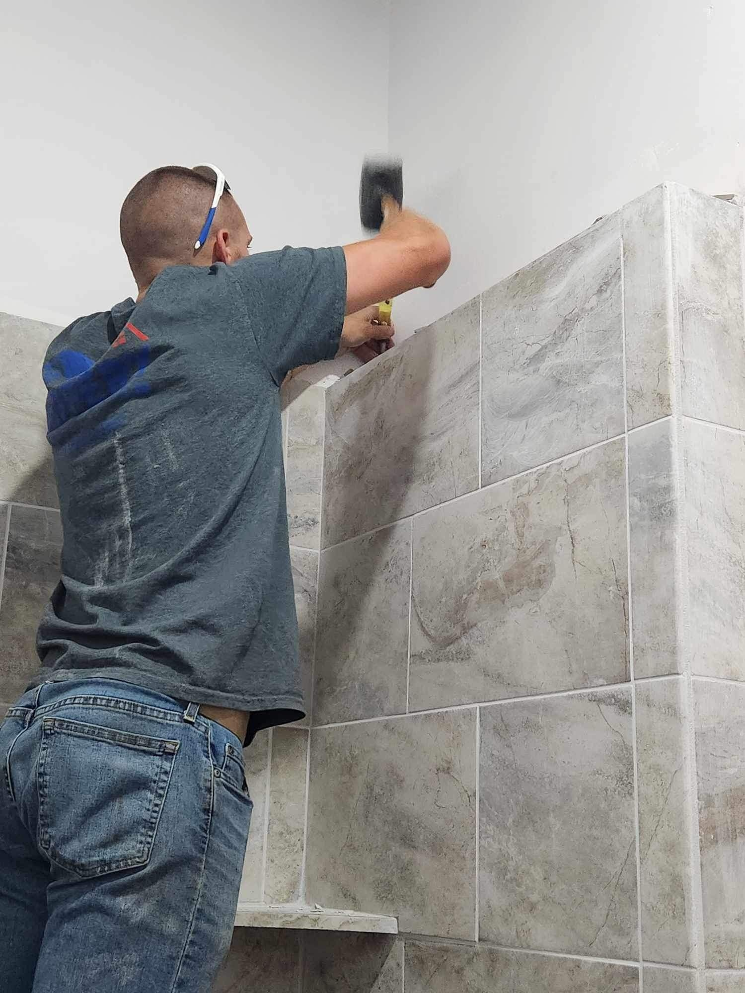 A person installing tile in a shower, using a hammer.