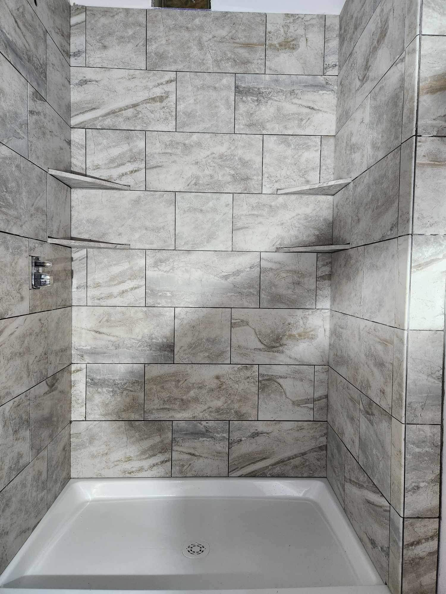 Gray tiled shower with built-in shelves. White shower base.