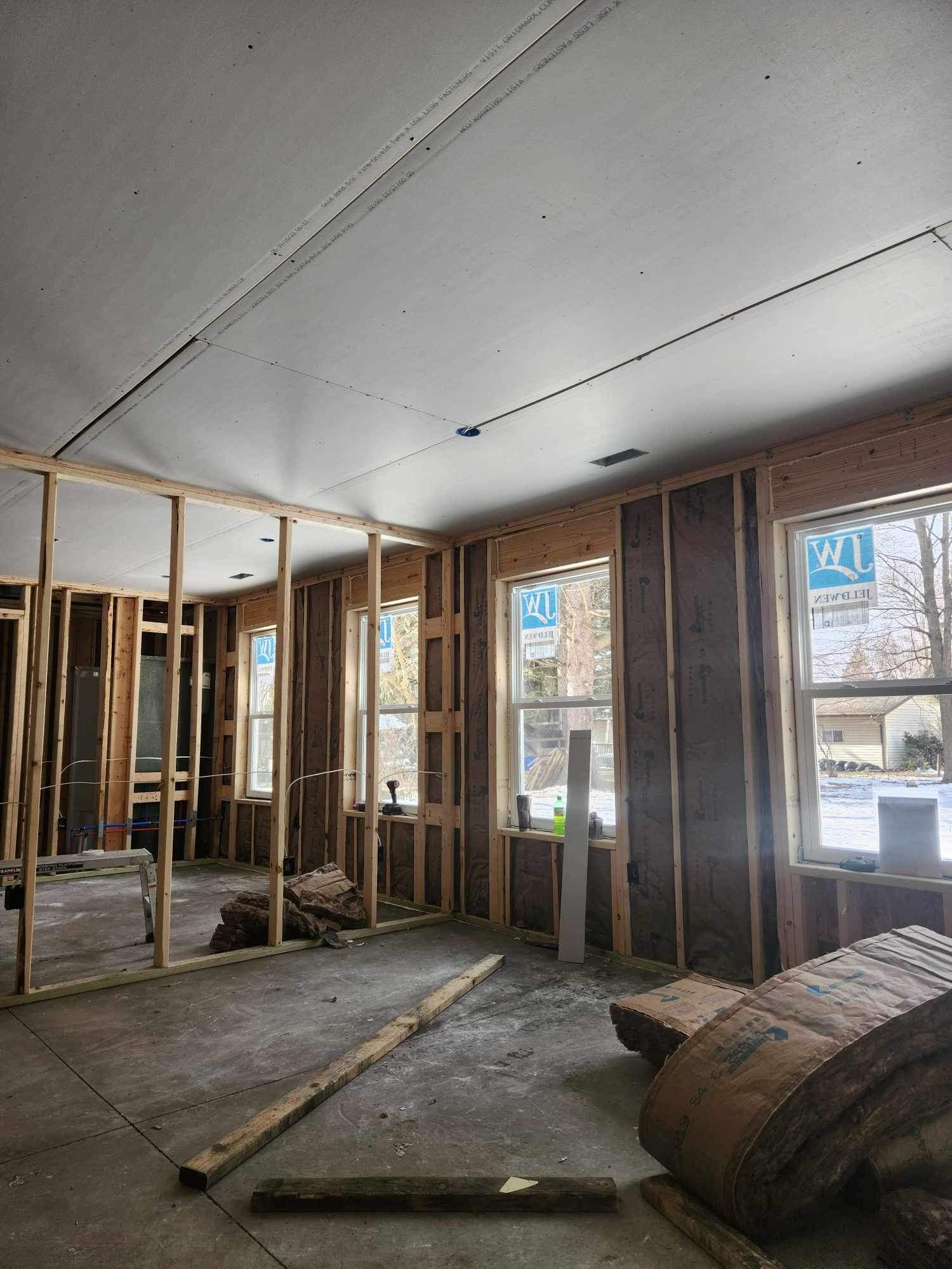Interior of a building under construction. Stud walls, windows, insulation, and drywall are visible.