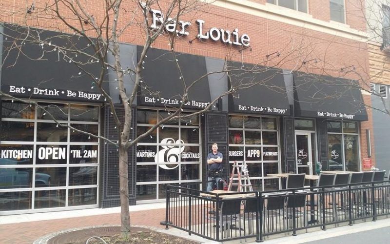 A man stands in front of a restaurant called far louie