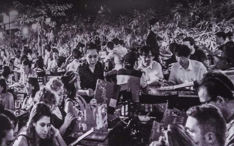 A black and white photo of a crowd of people sitting at tables.