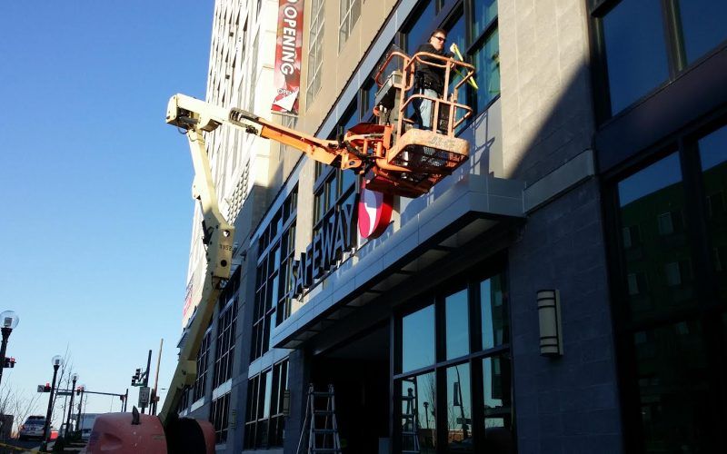 A man in a bucket is installing a sign on the side of a building