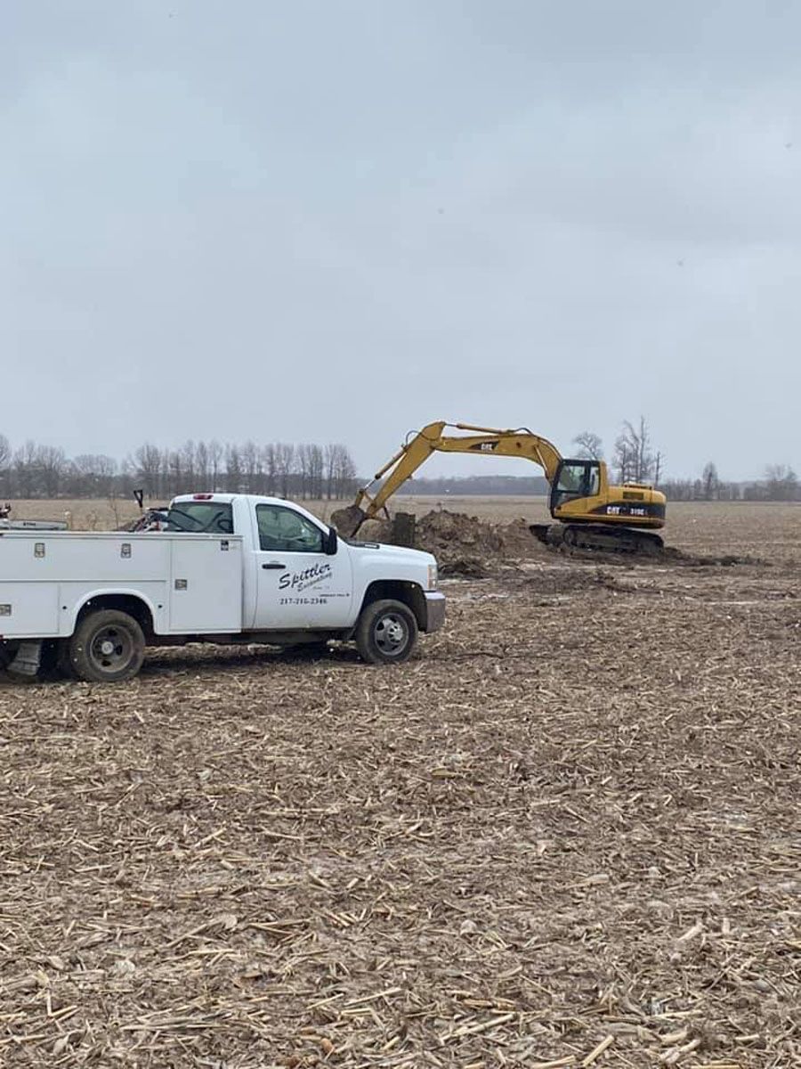 A white truck is parked in a field next to an excavator.