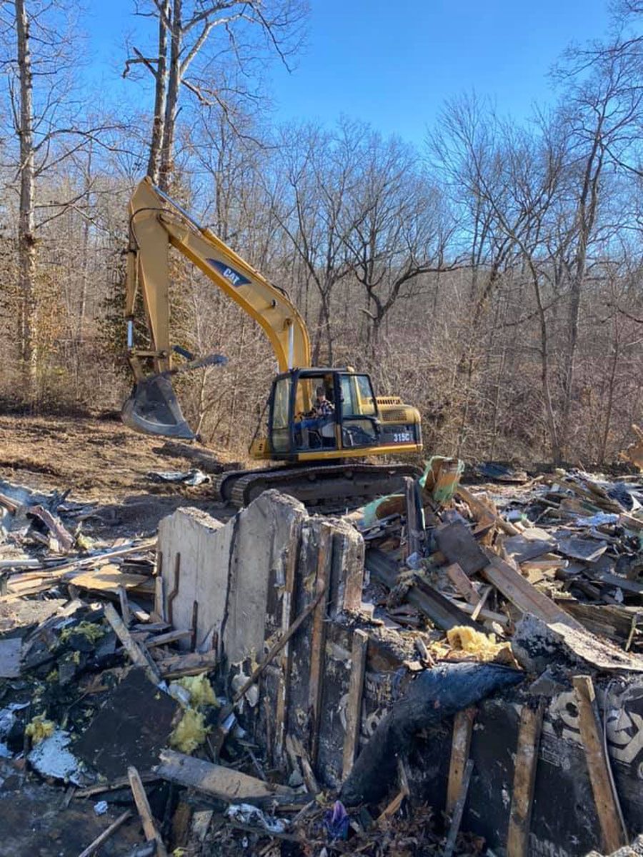 A yellow excavator is demolishing a building in the woods.