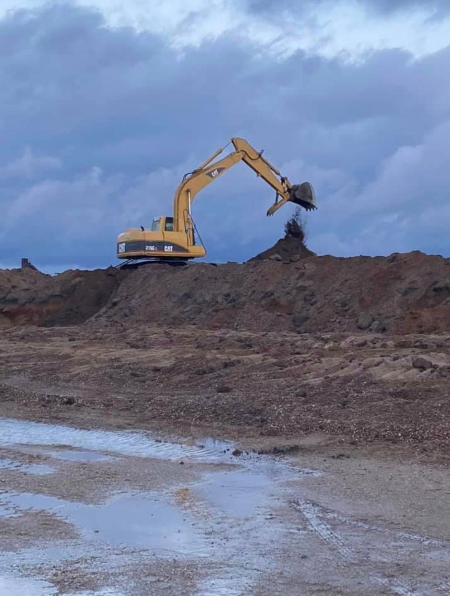 A yellow excavator is digging in a pile of dirt.