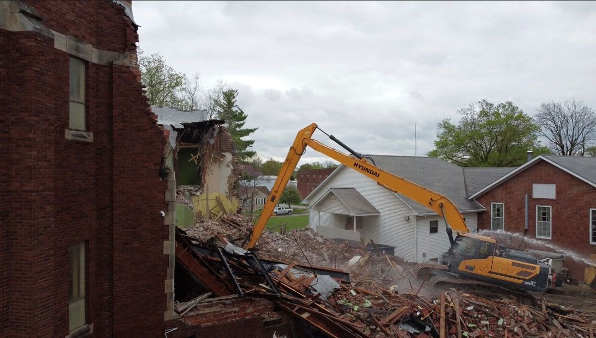 A large yellow excavator is demolishing a brick building.