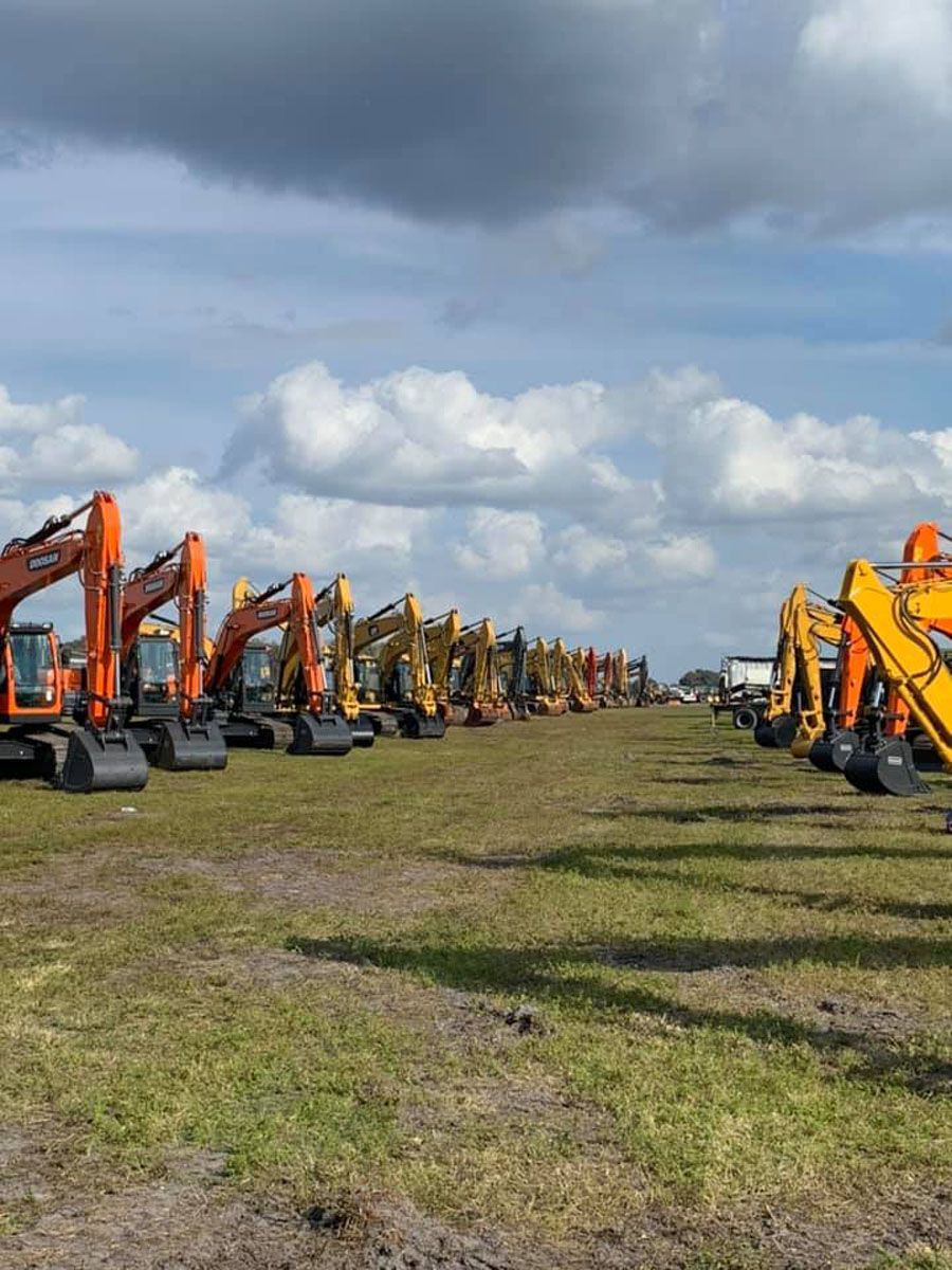 A row of orange and yellow excavators are parked in a grassy field.