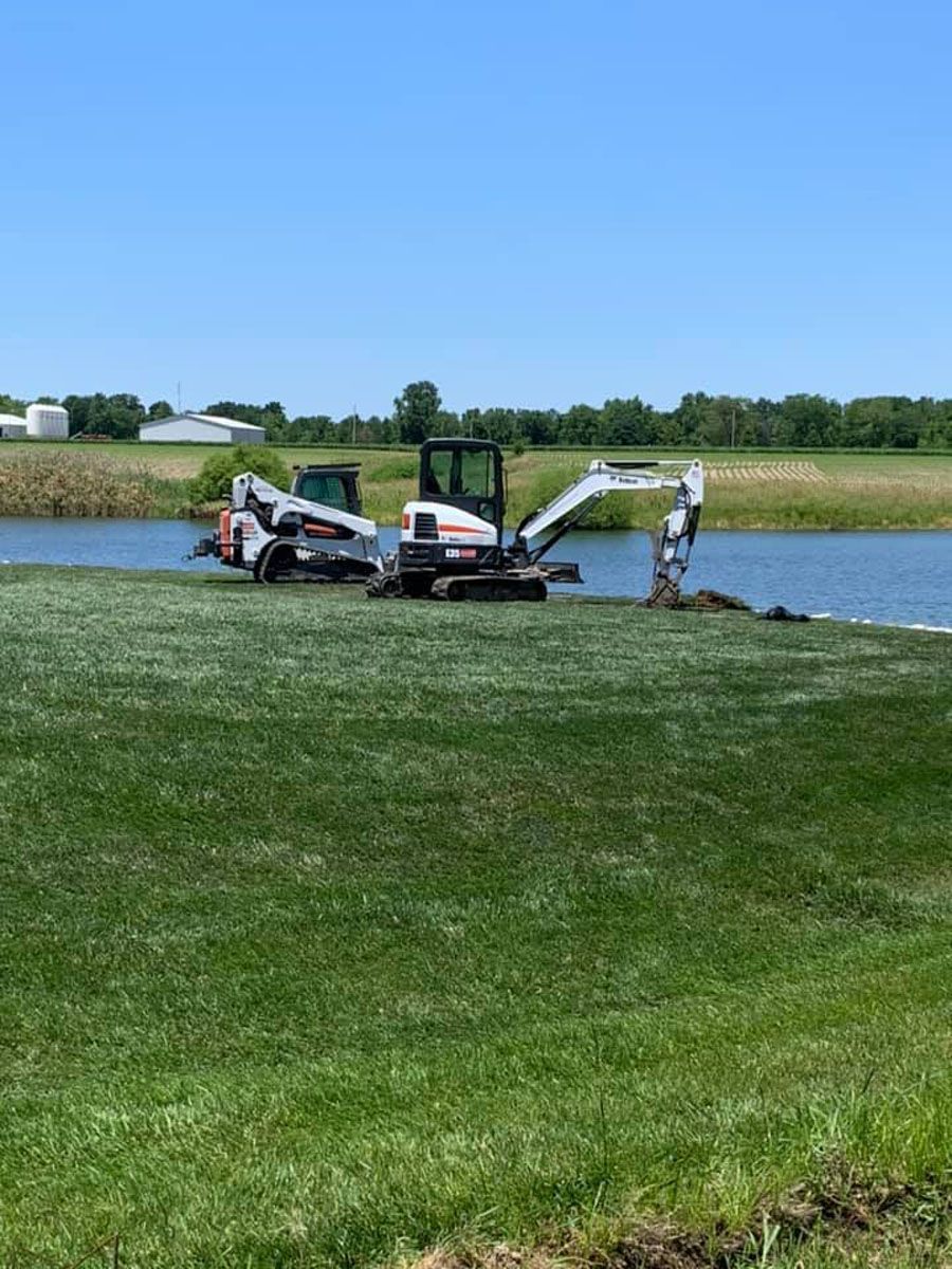 A bulldozer is sitting on top of a lush green field next to a body of water.
