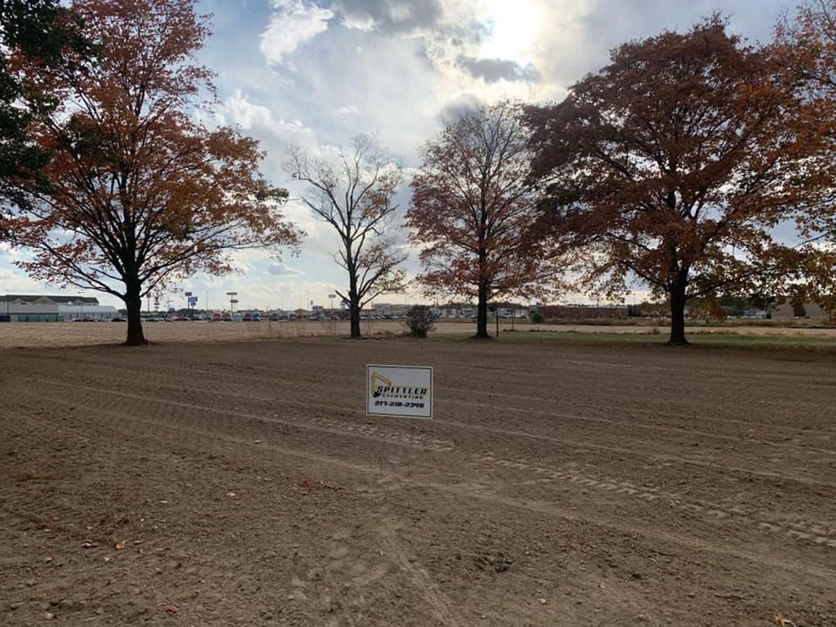 A dirt field with trees in the background and a sign in the middle