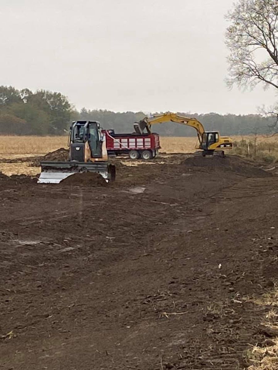A bulldozer is loading dirt into a dump truck in a field.