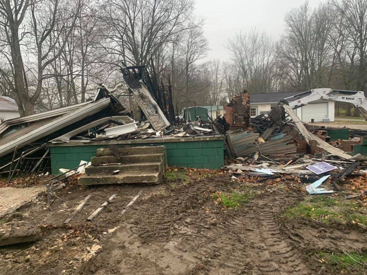 A house is being demolished in the middle of a dirt field.