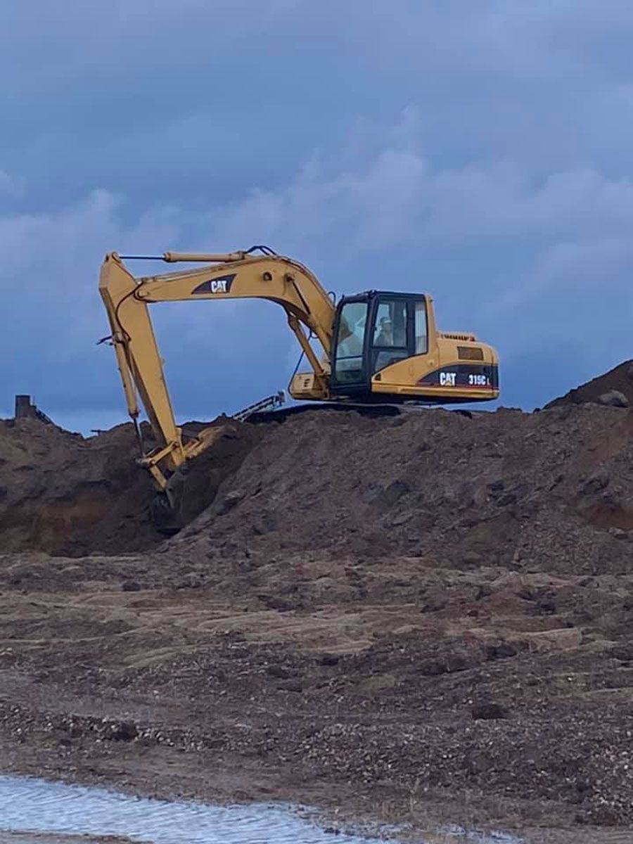 A yellow excavator is sitting on top of a pile of dirt.