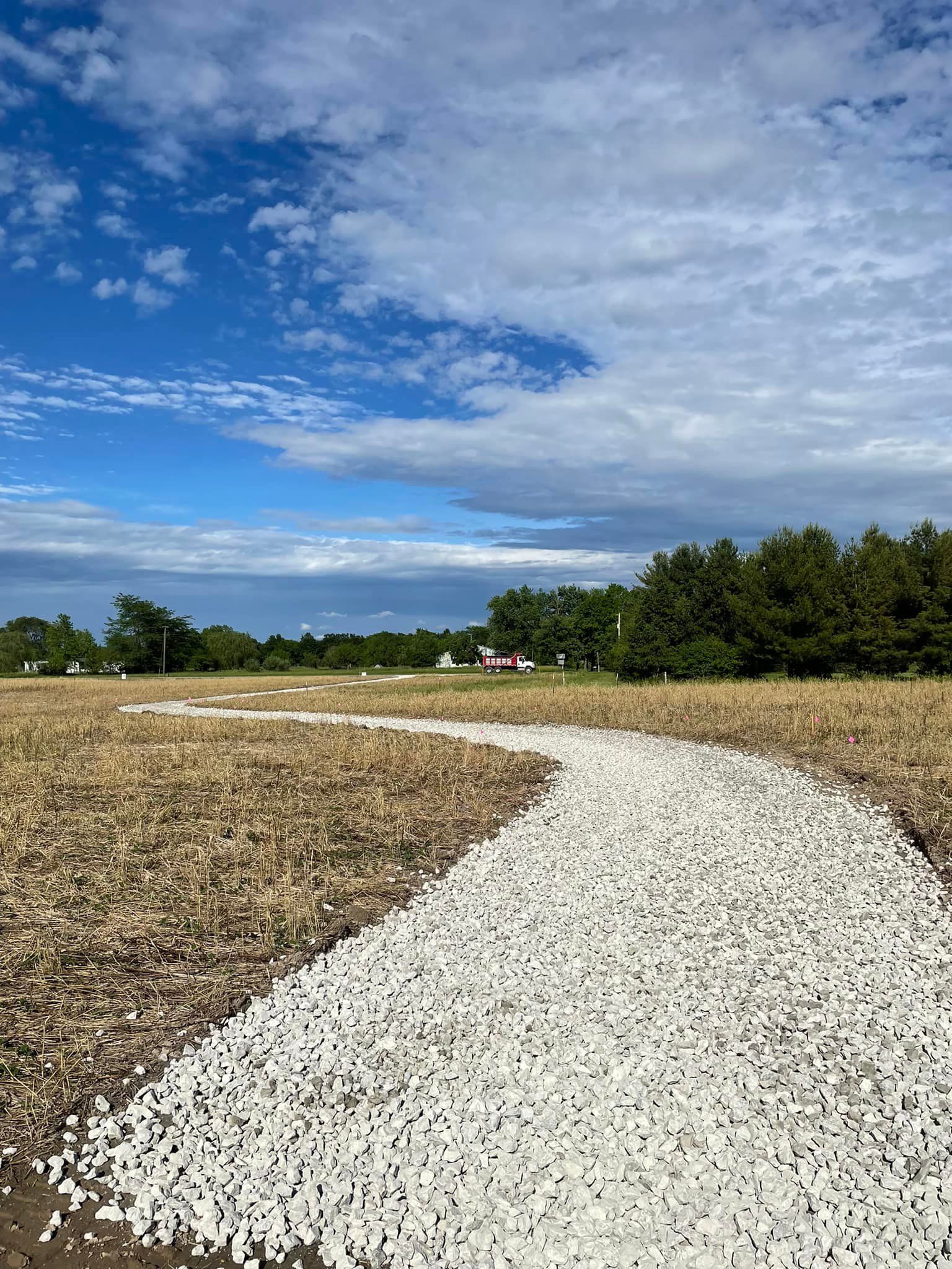 A path made of white gravel is going through a field.
