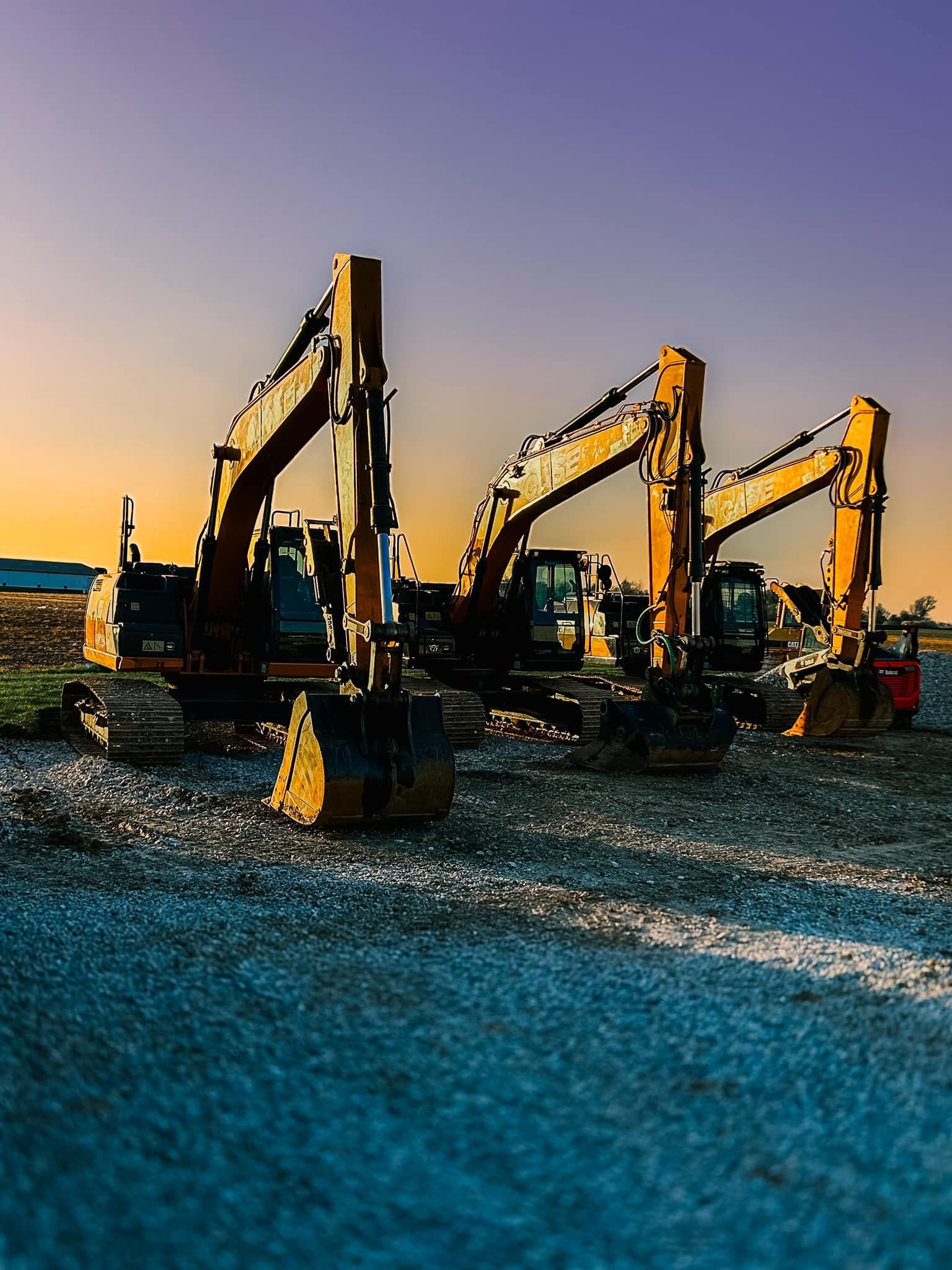 A row of construction vehicles are parked on a dirt road.