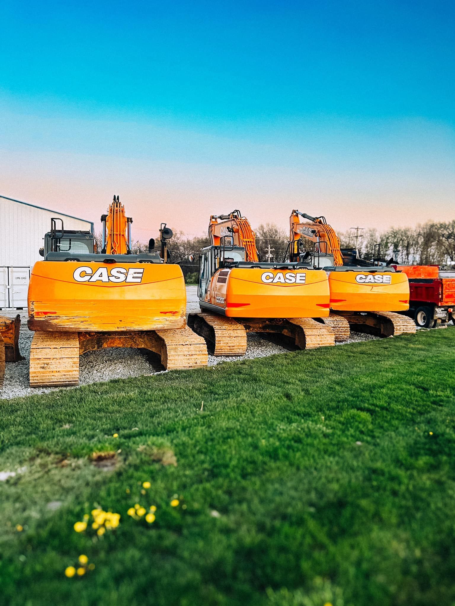 A row of case excavators are parked in a grassy field.
