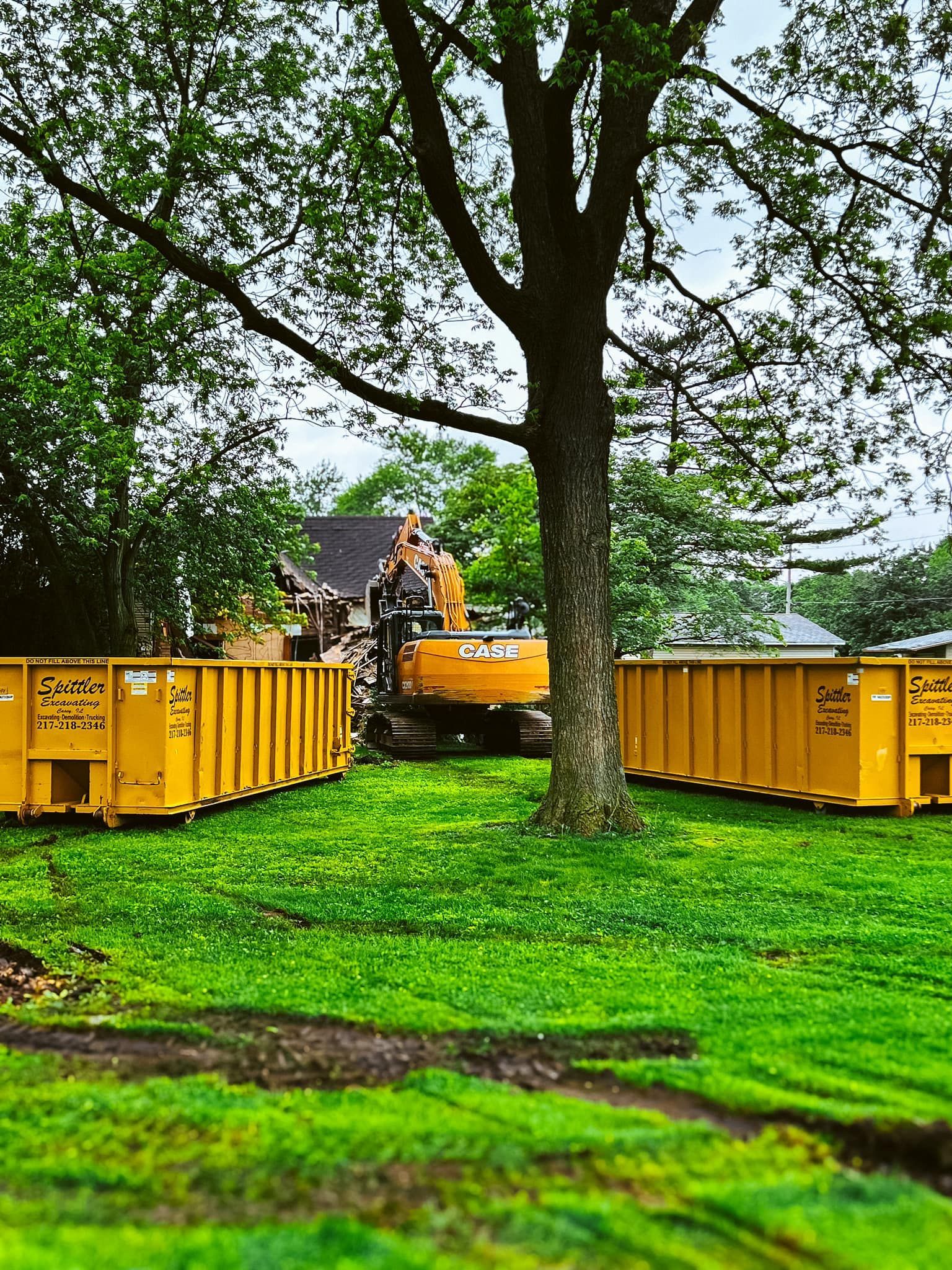 A yellow dumpster is sitting in the middle of a grassy field next to a tree.