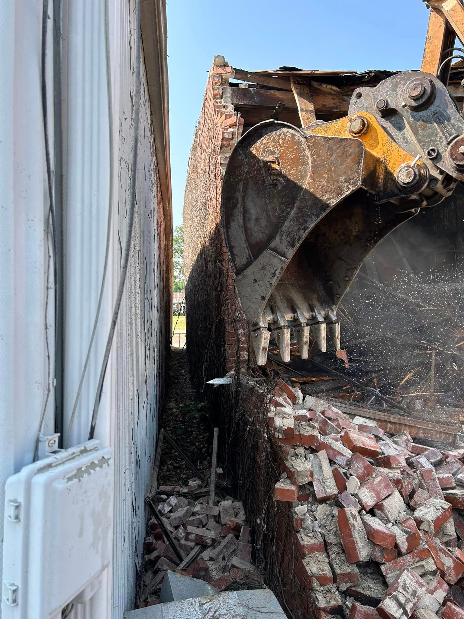 A brick wall is being demolished by a bulldozer.