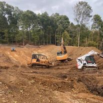 A group of construction vehicles are working on a dirt field.