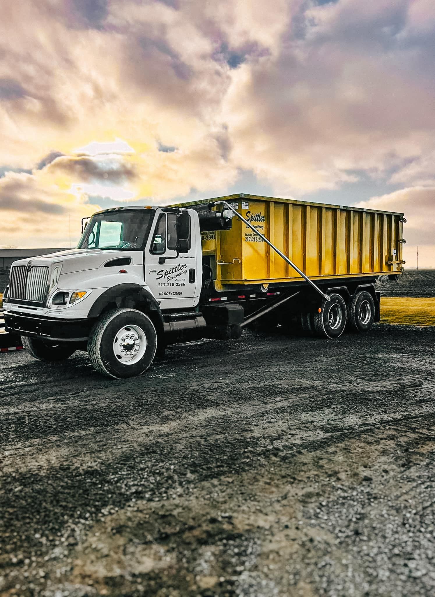 A yellow dump truck is parked in a gravel lot.