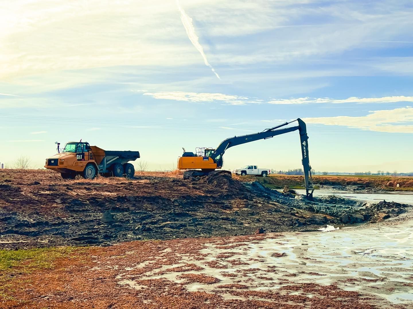 A dump truck and an excavator are working on a construction site next to a body of water.