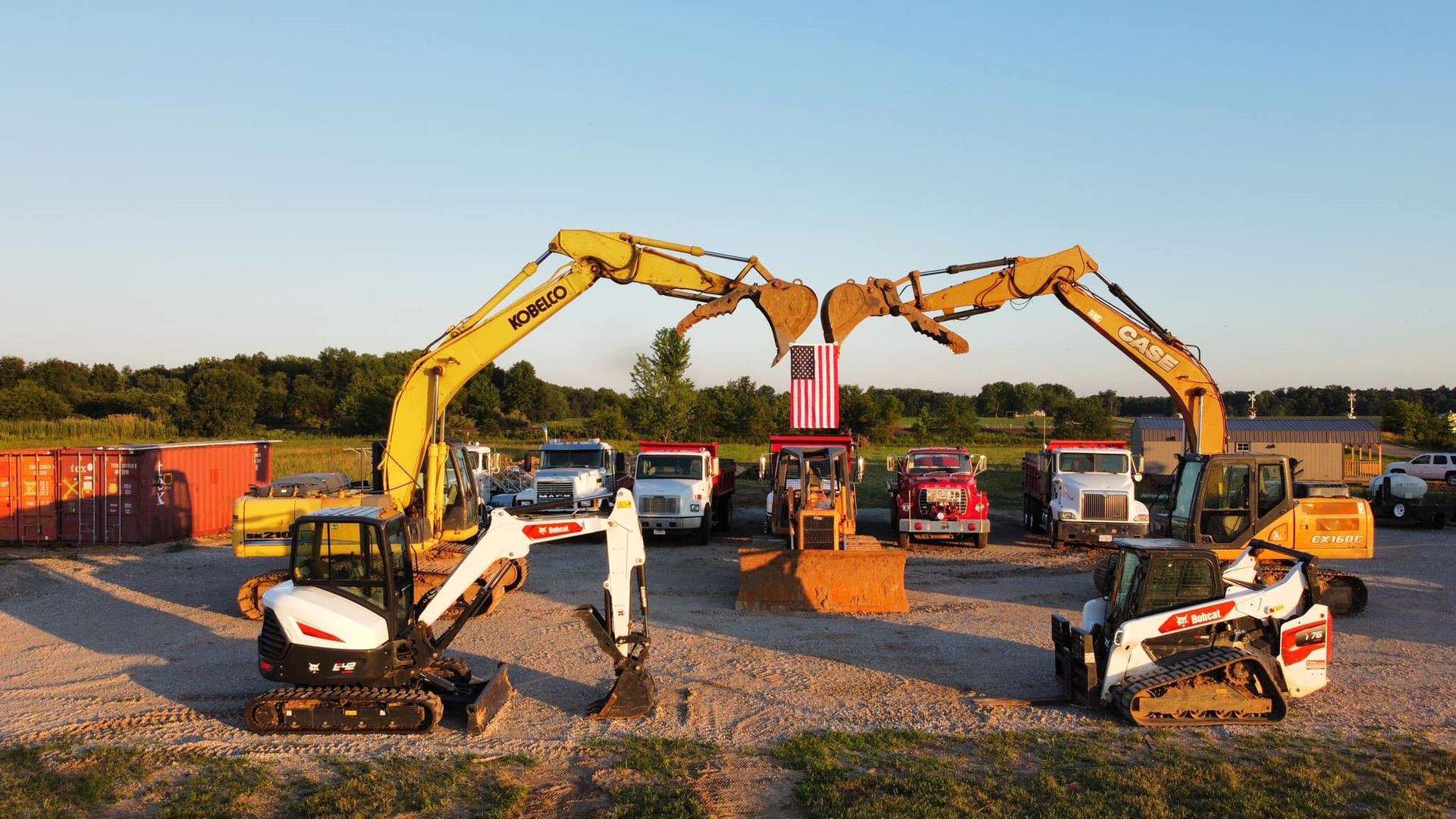 A group of construction vehicles are parked in a gravel lot.