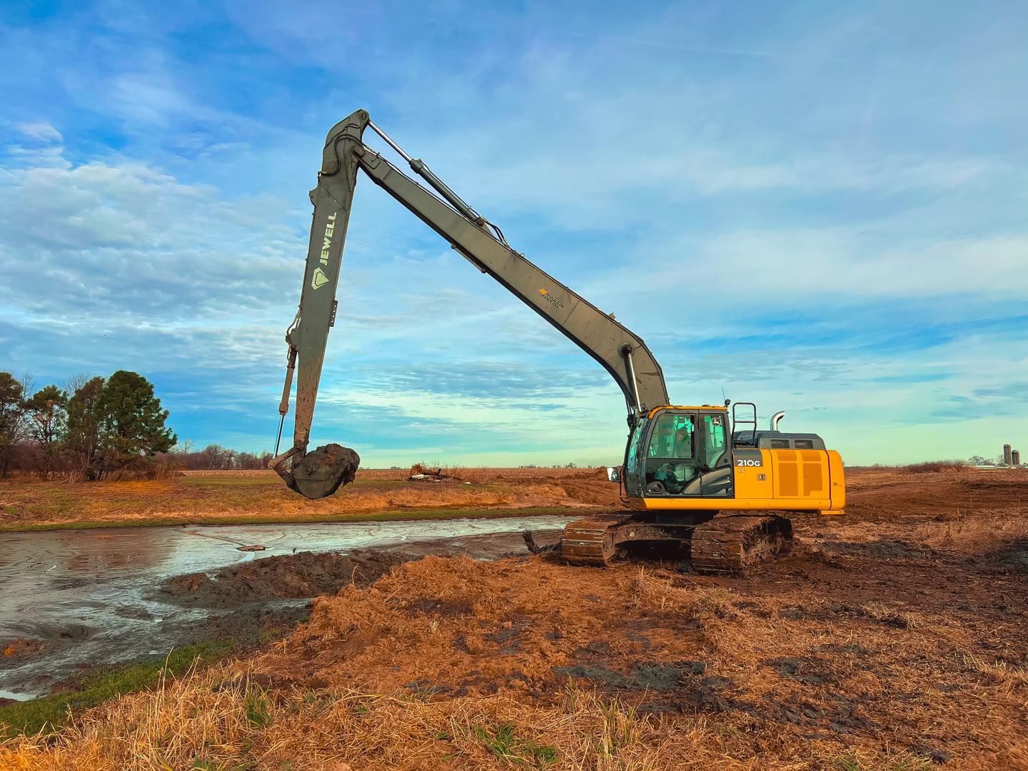 A large yellow excavator is digging a hole in a field next to a body of water.