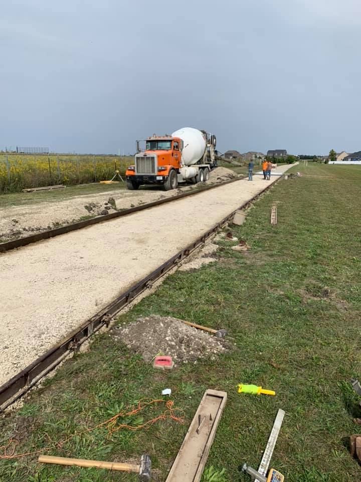 A concrete mixer truck is driving down a dirt road.