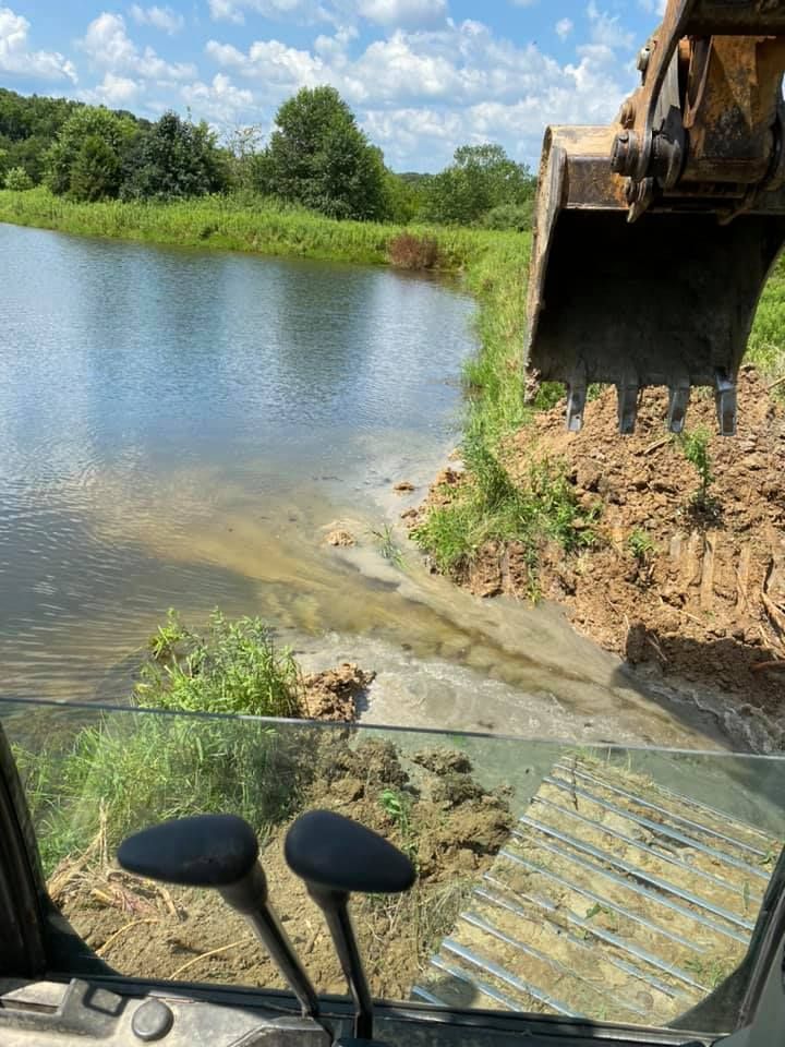 A bulldozer is digging a hole in the ground next to a lake.