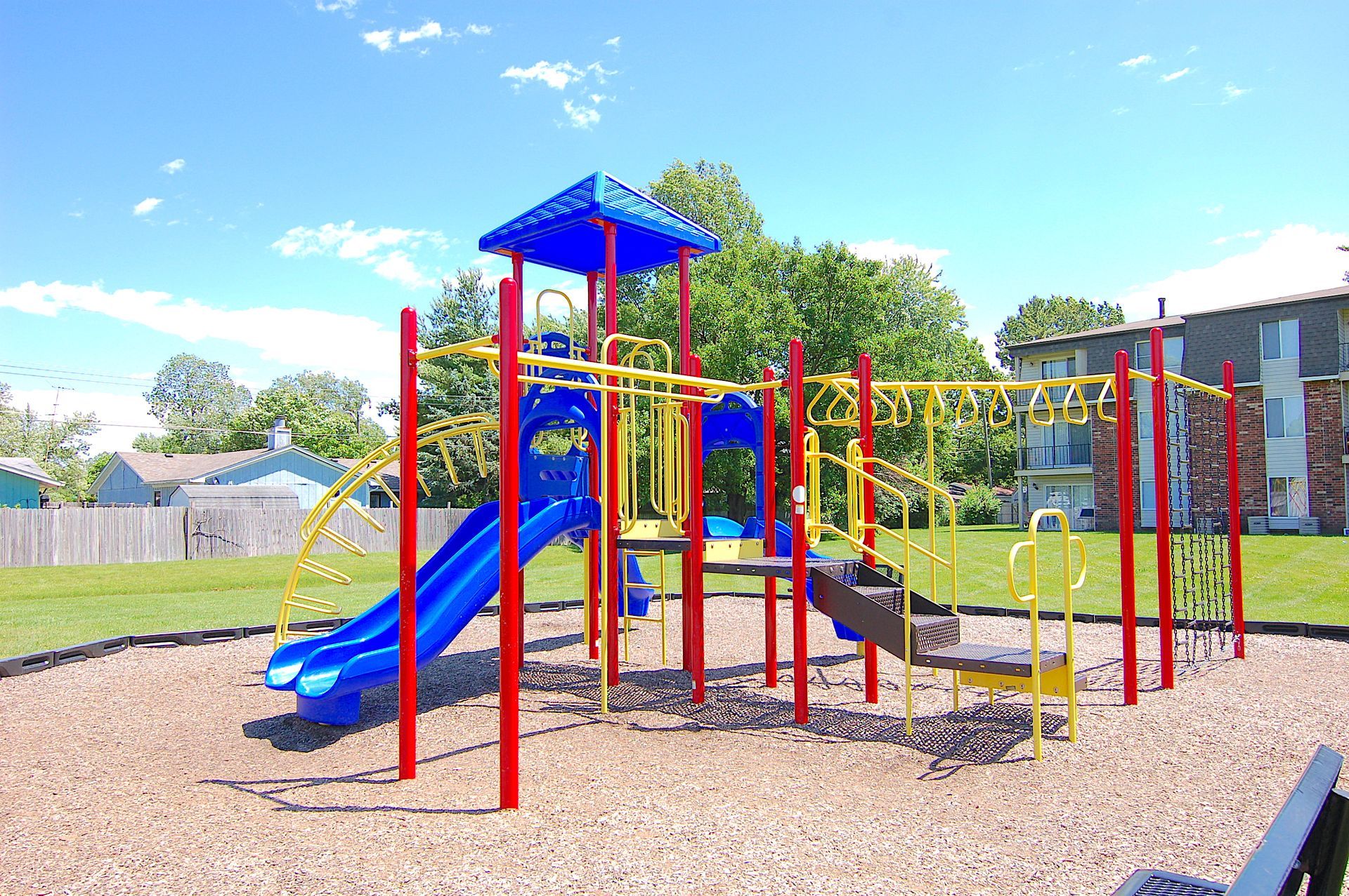 Colorful playground with blue slides, red climbing poles, and a yellow-roof play structure under a bright sky