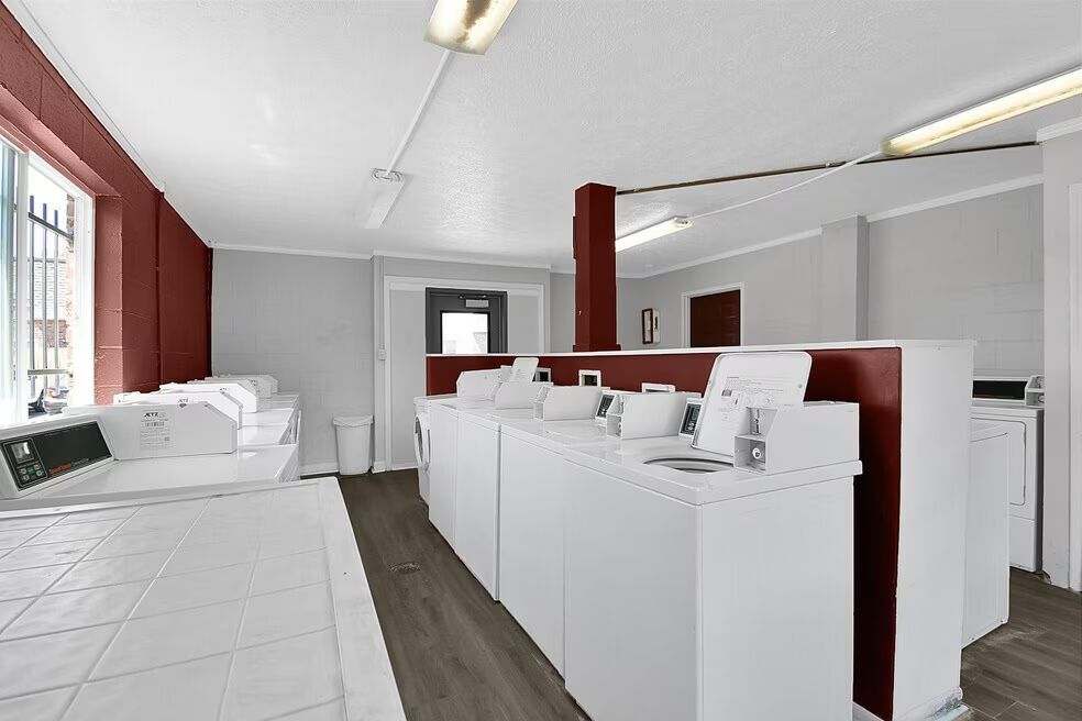 Bright laundry room with white washing machines, red accents, and laundry counters under fluorescent lights