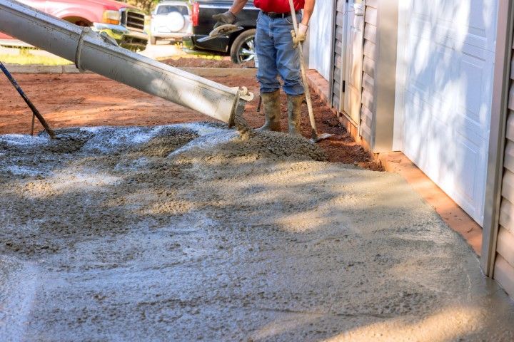 Concrete being poured from a chute onto a driveway by a person in boots.