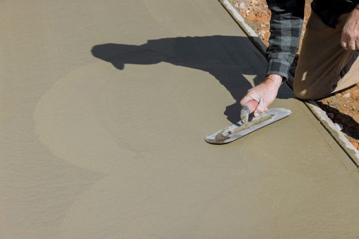 Person smoothing fresh concrete with a trowel outdoors.