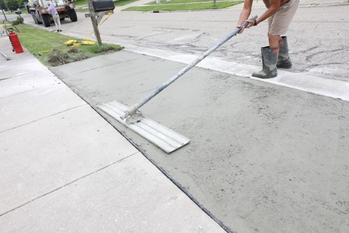 Person smoothing wet concrete sidewalk with a long-handled float tool.