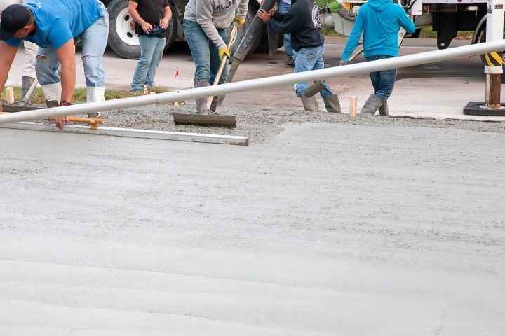 Construction workers pouring and leveling wet concrete on a paved surface.