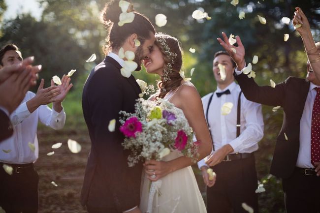 A bride and groom are kissing in front of their wedding party.