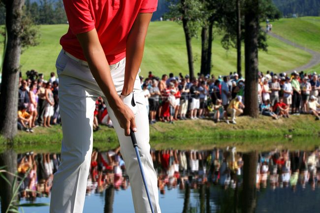 A man in a red shirt is swinging a golf club on a golf course.
