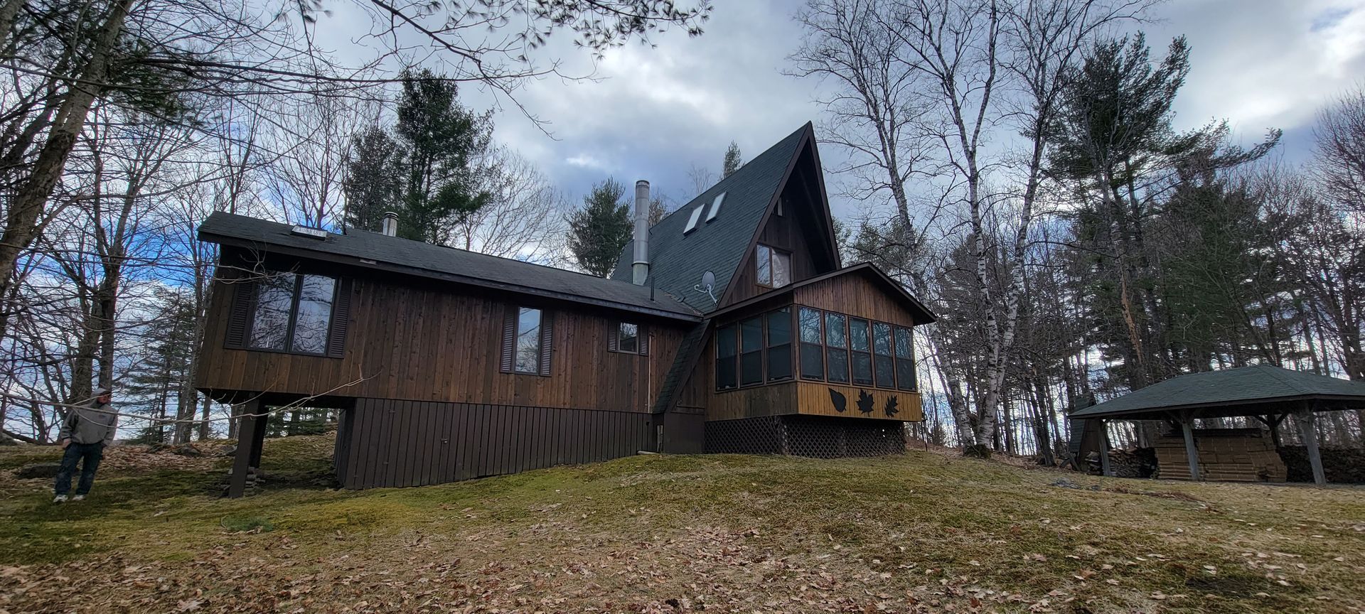 A large wooden house is sitting on top of a hill in the middle of a forest.