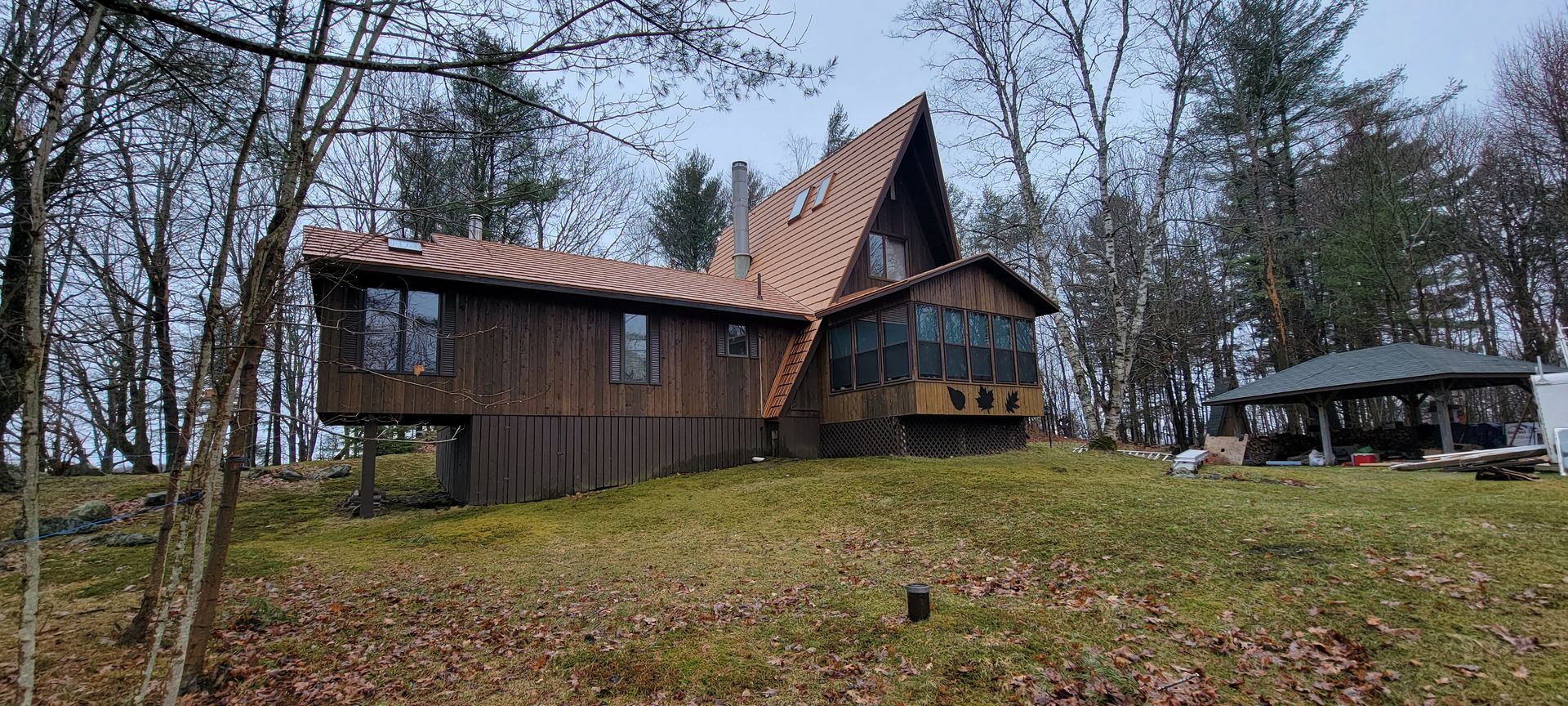 A large wooden house is sitting on top of a grassy hill in the middle of a forest.