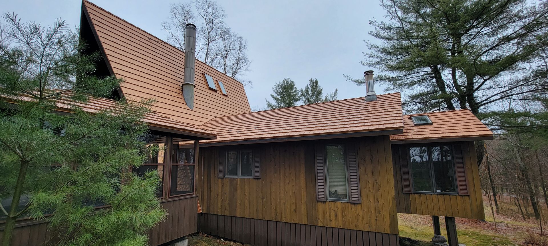 A wooden house with a copper roof in the middle of a forest.
