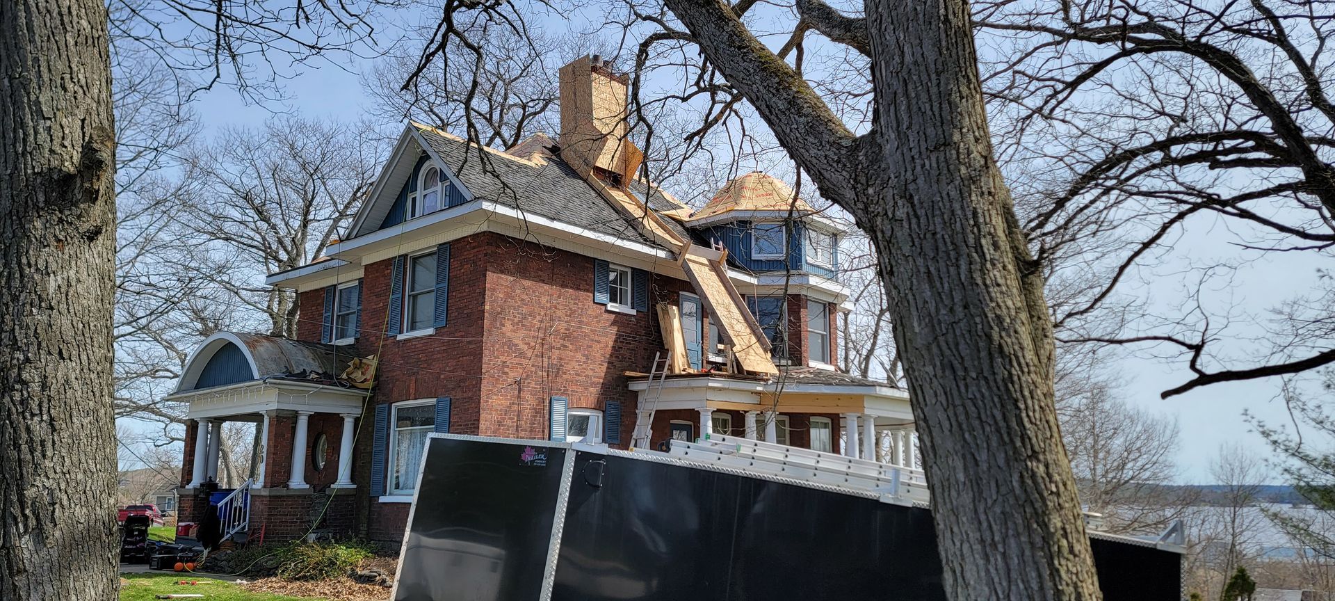 A large brick house with a roof that has been damaged by a tree.