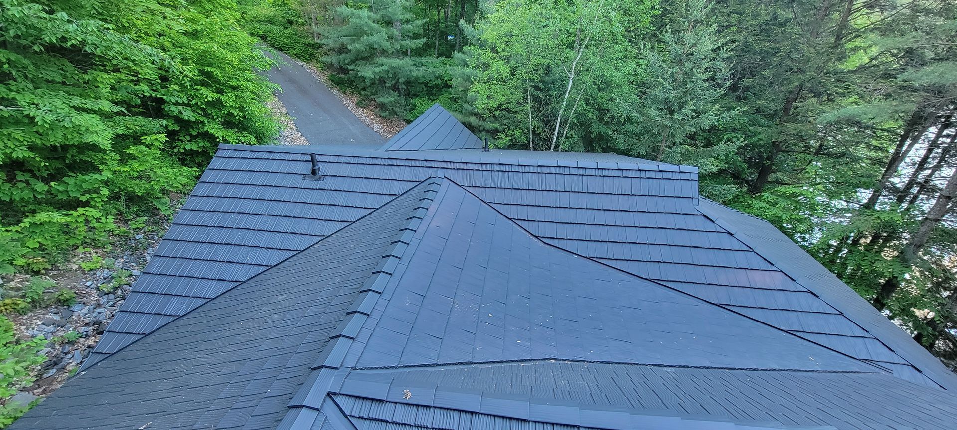 The roof of a house is surrounded by trees and a road.
