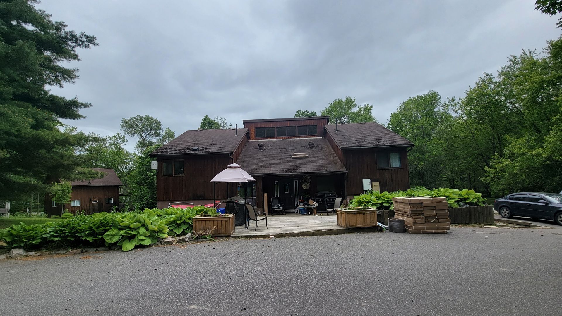 A large wooden house is surrounded by trees and a gravel driveway.